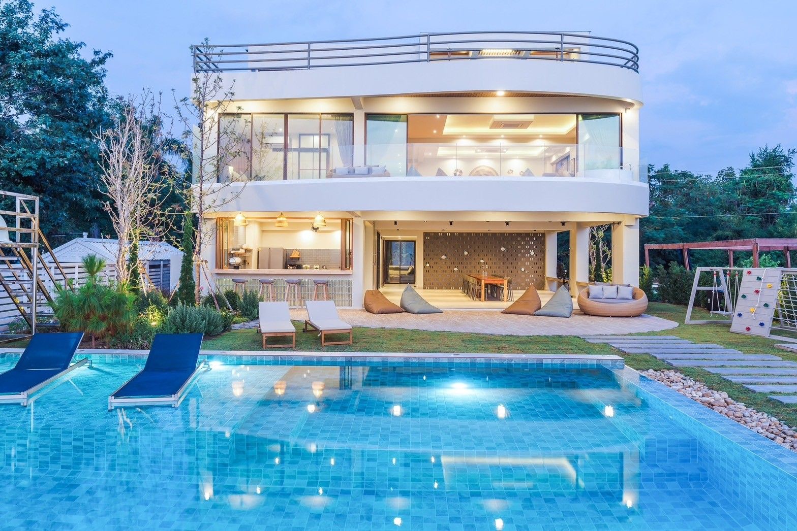 Evening view of the pool at All About VII Pool Villa, near Bangket Beach, Cha-am. Loungers and outdoor kitchen visible.