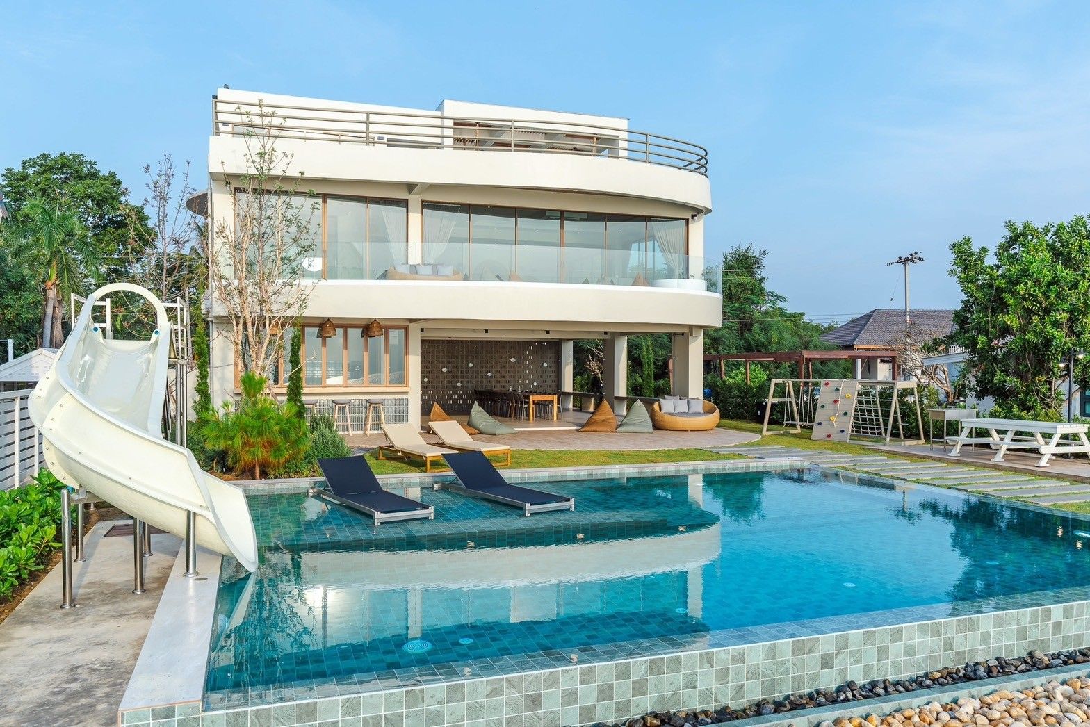 All About VII Pool Villa, Cha Am, with water slide into the turquoise pool. Loungers and outdoor seating visible.