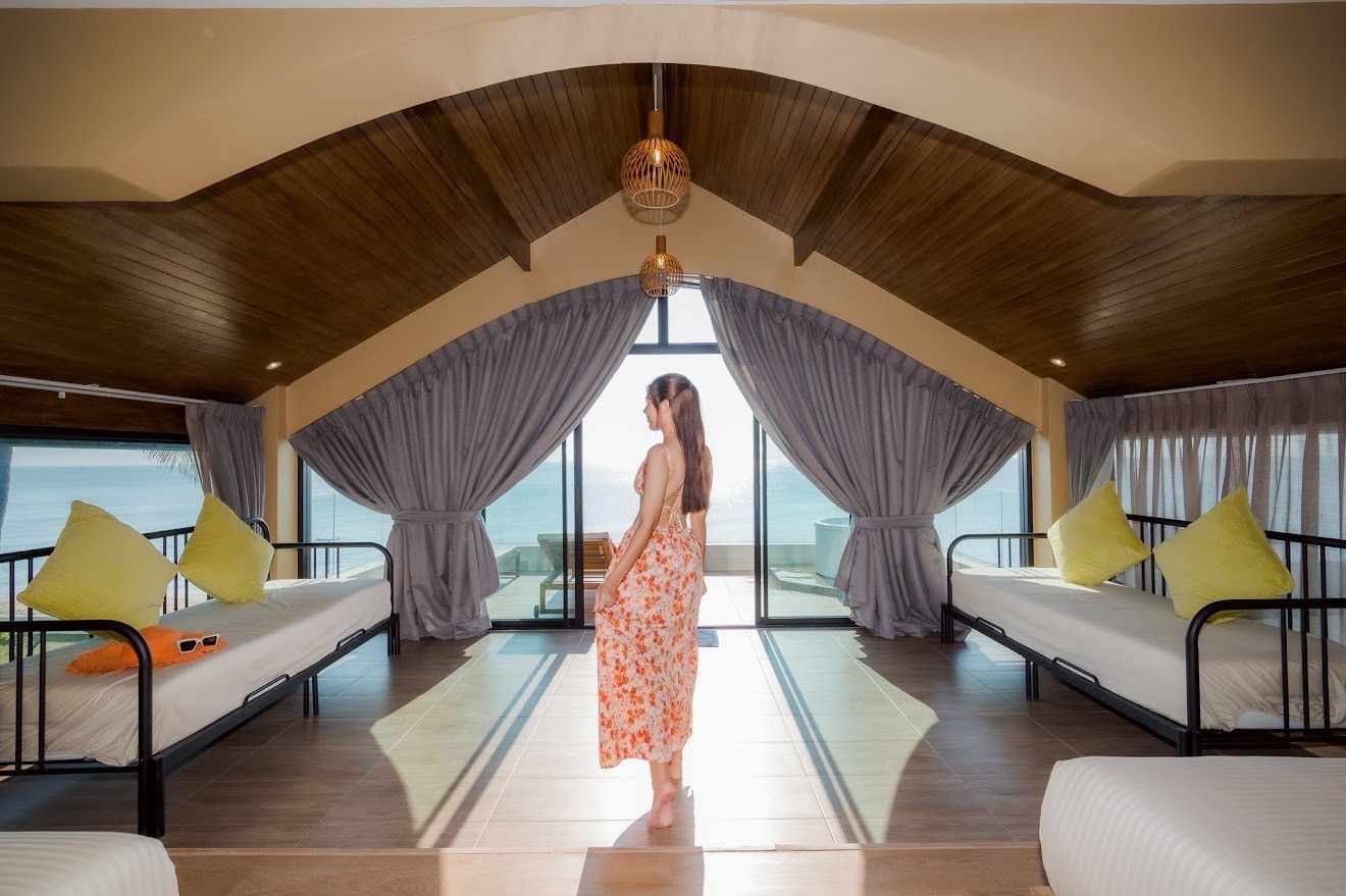 Bright bedroom with twin beds and ocean view at Beach Mood VI Pool Villa, หาดบางเกตุ ชะอำ. Woman in dress standing.