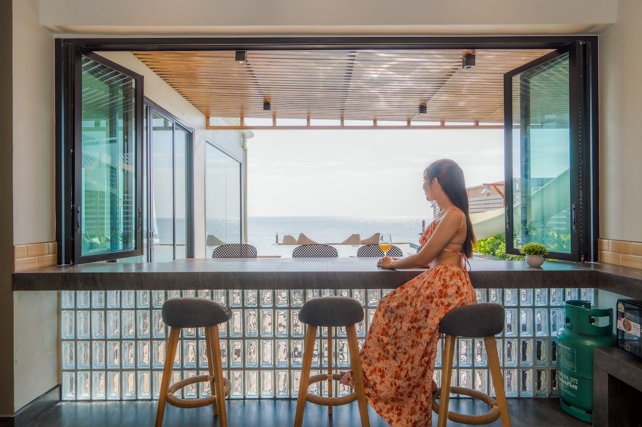 Woman at indoor-outdoor bar with ocean view at Beach Mood VI Pool Villa, หาดบางเกตุ ชะอำ. Stools and glass block detail.