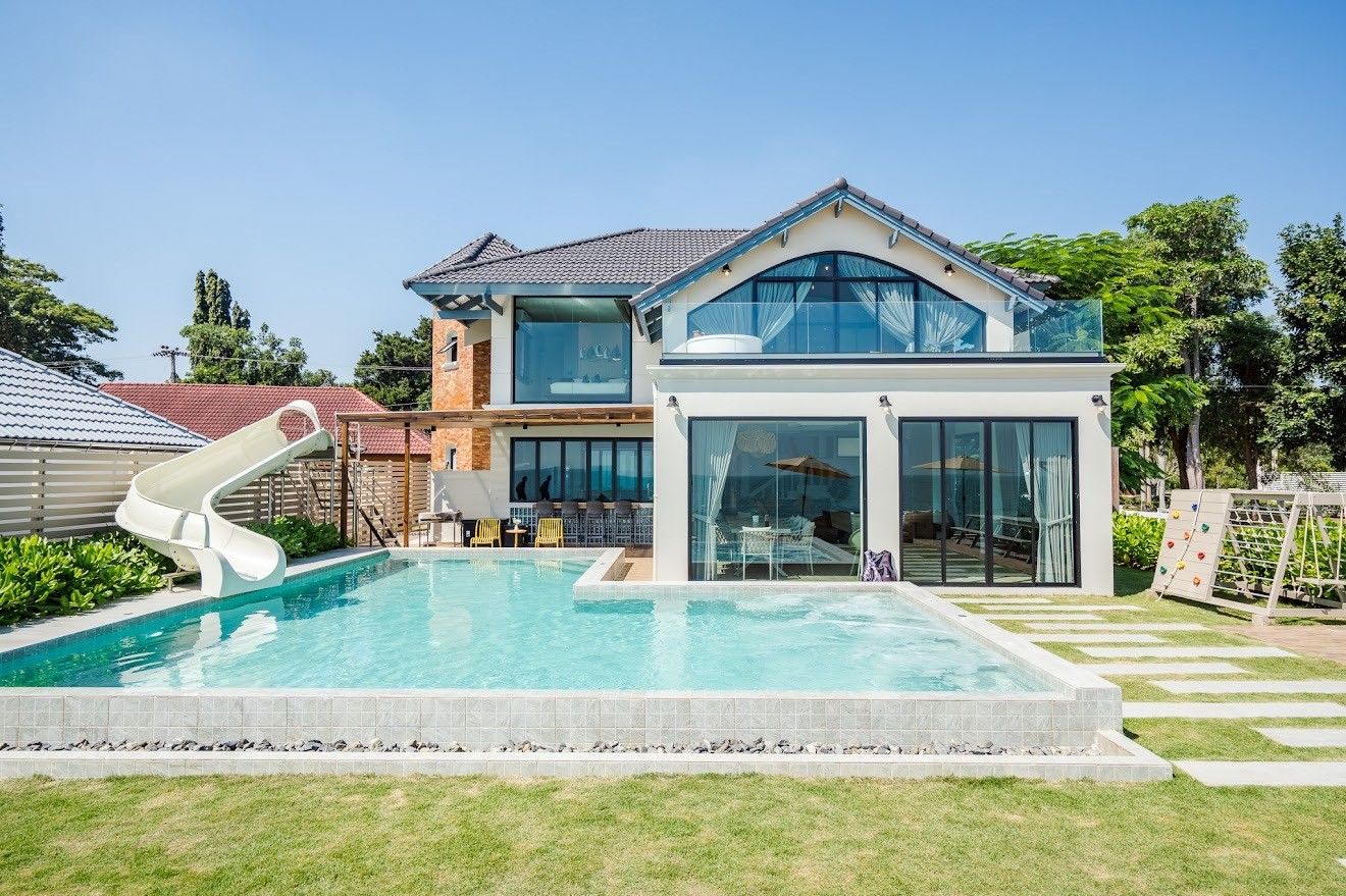 Beach Mood VI Pool Villa in Cha Am has a water slide into the pool. View of the villa exterior and pool from the lawn.