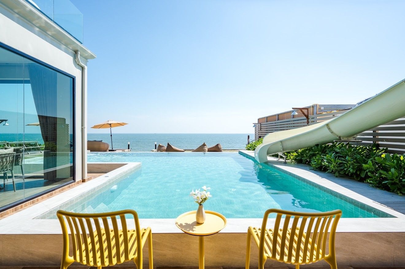 Beach Mood VI pool villa in หาดบางเกตุ ชะอำ features a pool with a water slide and yellow chairs overlooking the ocean.