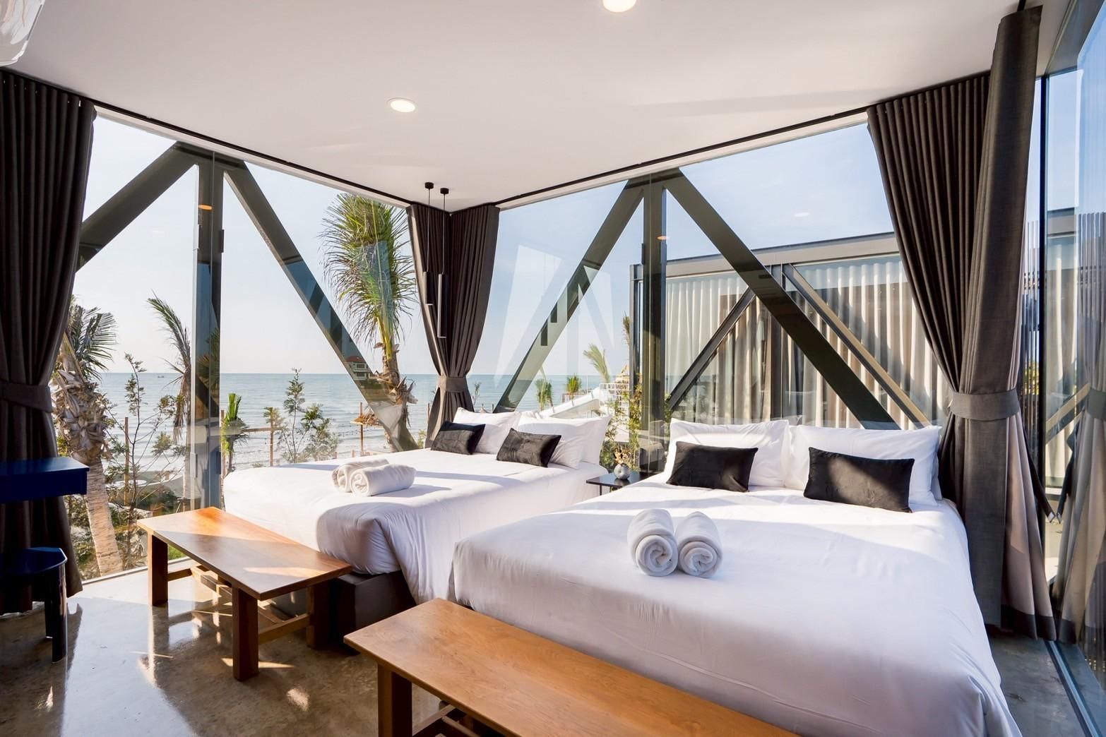 Bright bedroom at Beyond V Pool Villa, หาดปึกเตียน-ชะอำ, with two twin beds and ocean view through geometric windows.