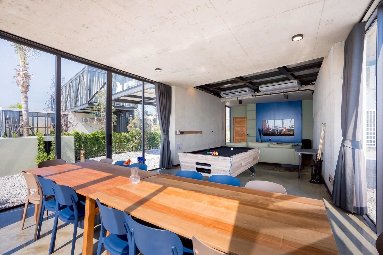 Dining area and pool table at Beyond V Pool Villa, หาดปึกเตียน-ชะอำ. Long wooden table with blue chairs, view to the outside.