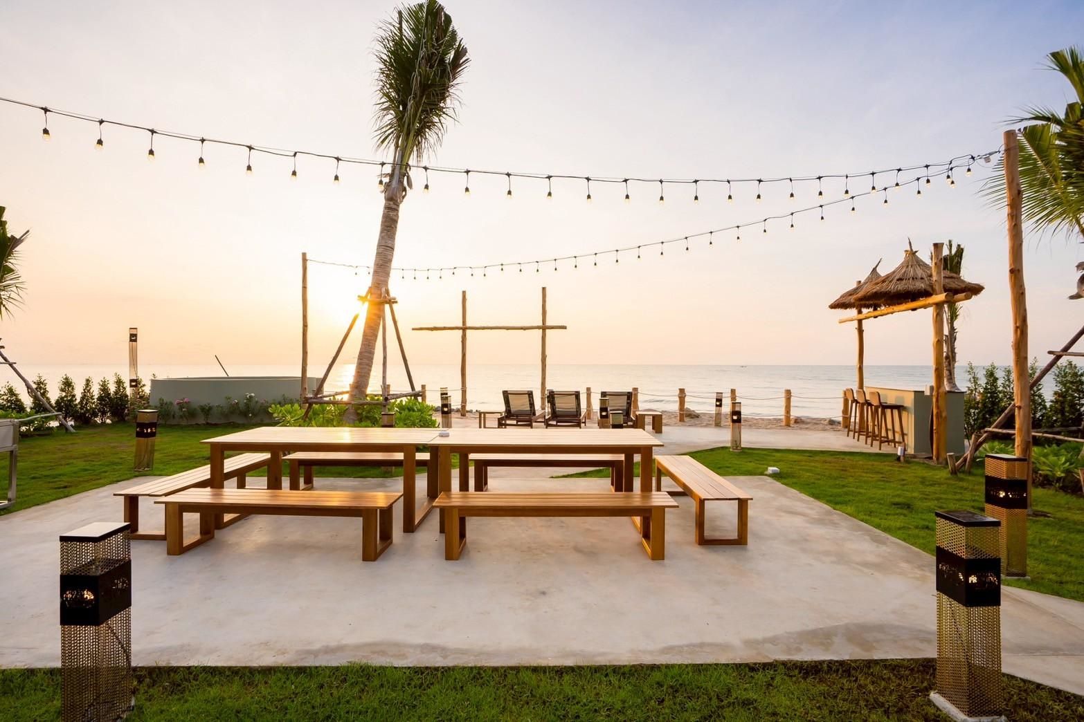 Beachfront dining at Beyond V Pool Villa, หาดปึกเตียน-ชะอำ. Outdoor tables and benches with sunset view.