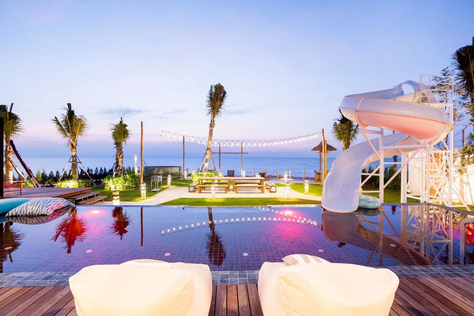 Beyond V Pool Villa pool view at dusk, Puk Tian Beach. Features a water slide and beachfront dining.
