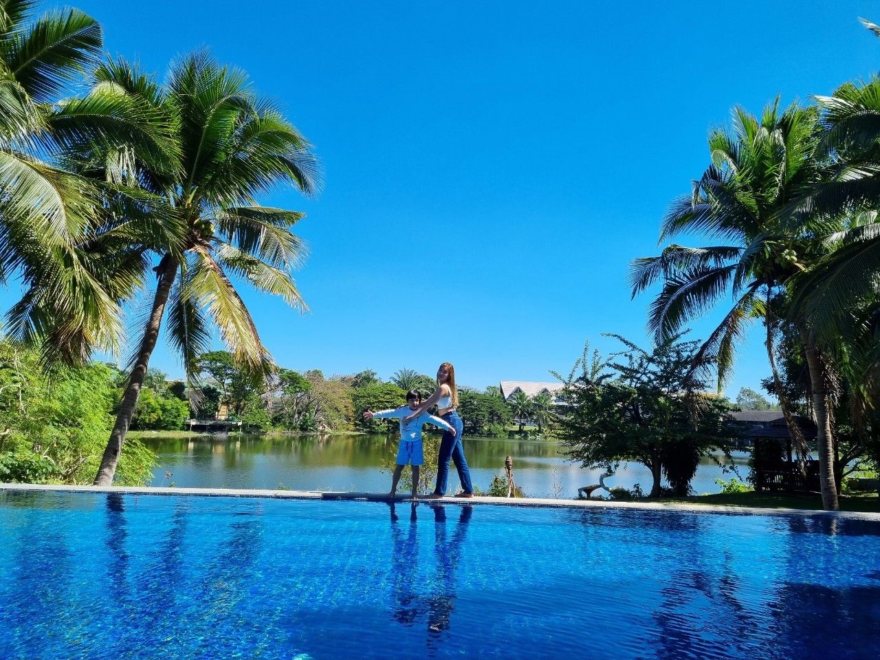 Guests enjoying the infinity pool with lake and palm views.