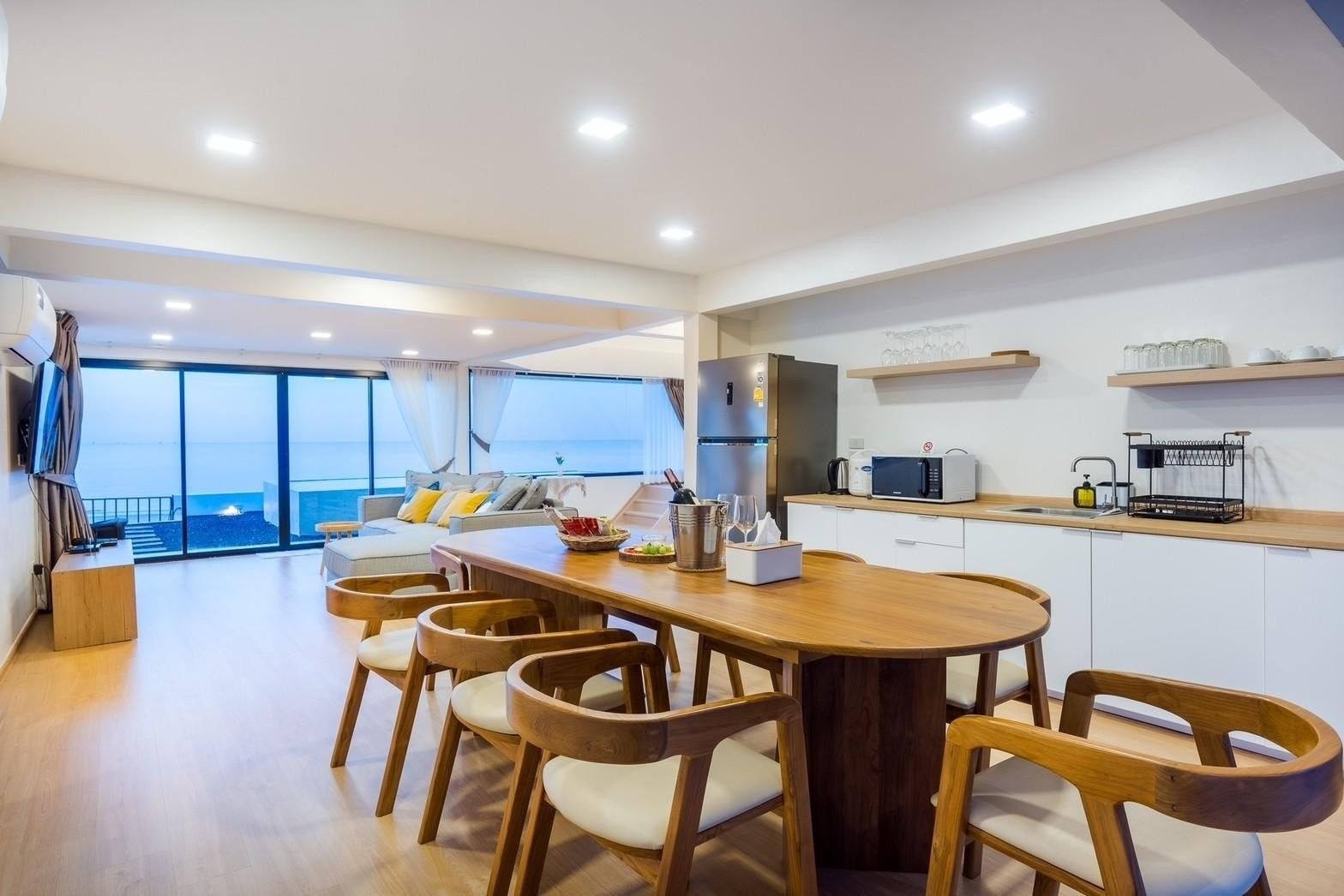 Dining area with ocean view at Costa IV Beachfront Pool Villa, Cha-am, Phetchaburi. Wooden table with chairs, kitchen in back