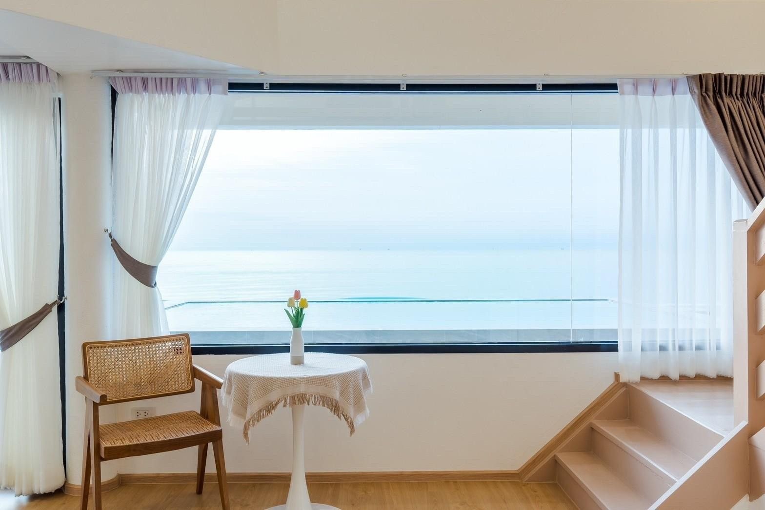 Ocean view from Costa IV Beachfront Pool Villa, ชะอำ เพชรบุรี. Rattan chair and small table with flowers in front of large wi