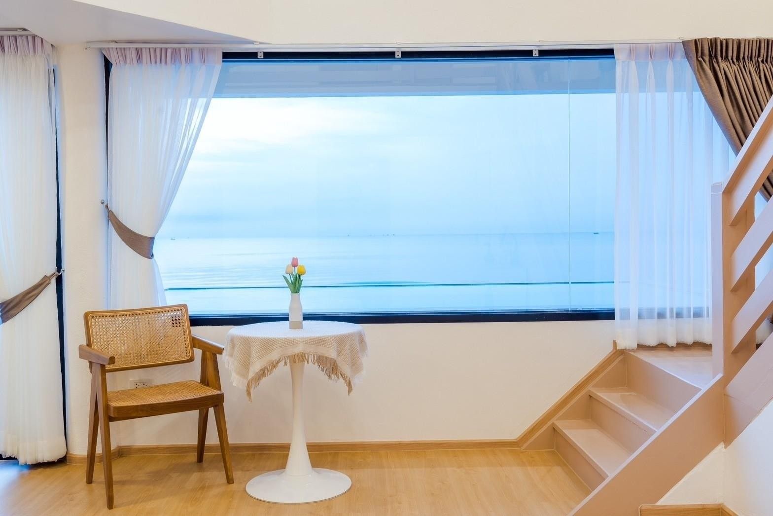 Ocean view seating area at Costa IV Beachfront Pool Villa, ชะอำ เพชรบุรี. Rattan chair and table with flowers by the window.