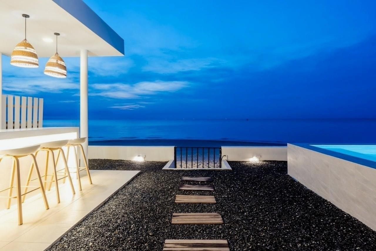 Costa IV Beachfront Pool Villa in ชะอำ เพชรบุรี features a bar with seating overlooking the ocean at dusk.