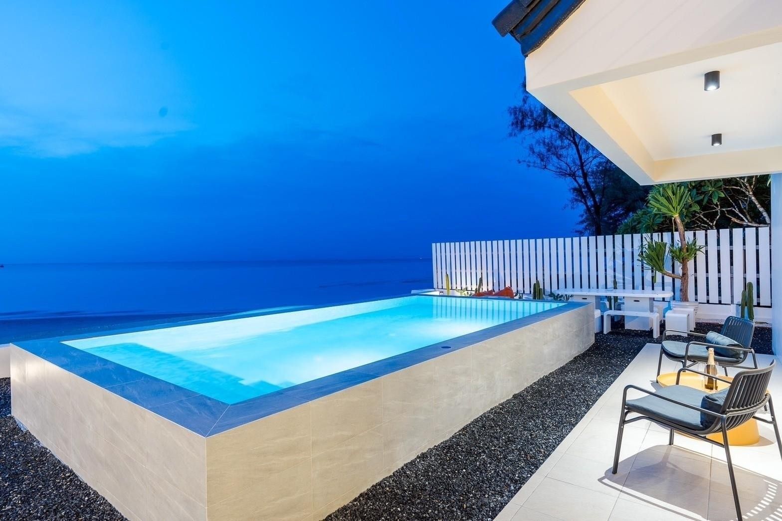 Costa IV Beachfront Pool Villa in ชะอำ เพชรบุรี features a stunning infinity pool overlooking the ocean at dusk.