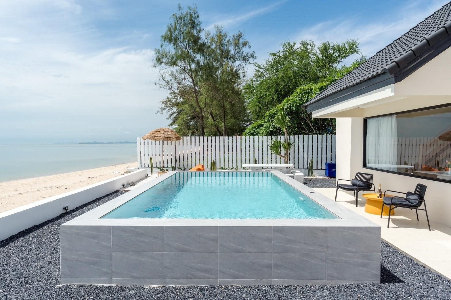 Costa IV beachfront pool villa in ชะอำ เพชรบุรี. View of the pool, beach, and chairs on the pool deck.