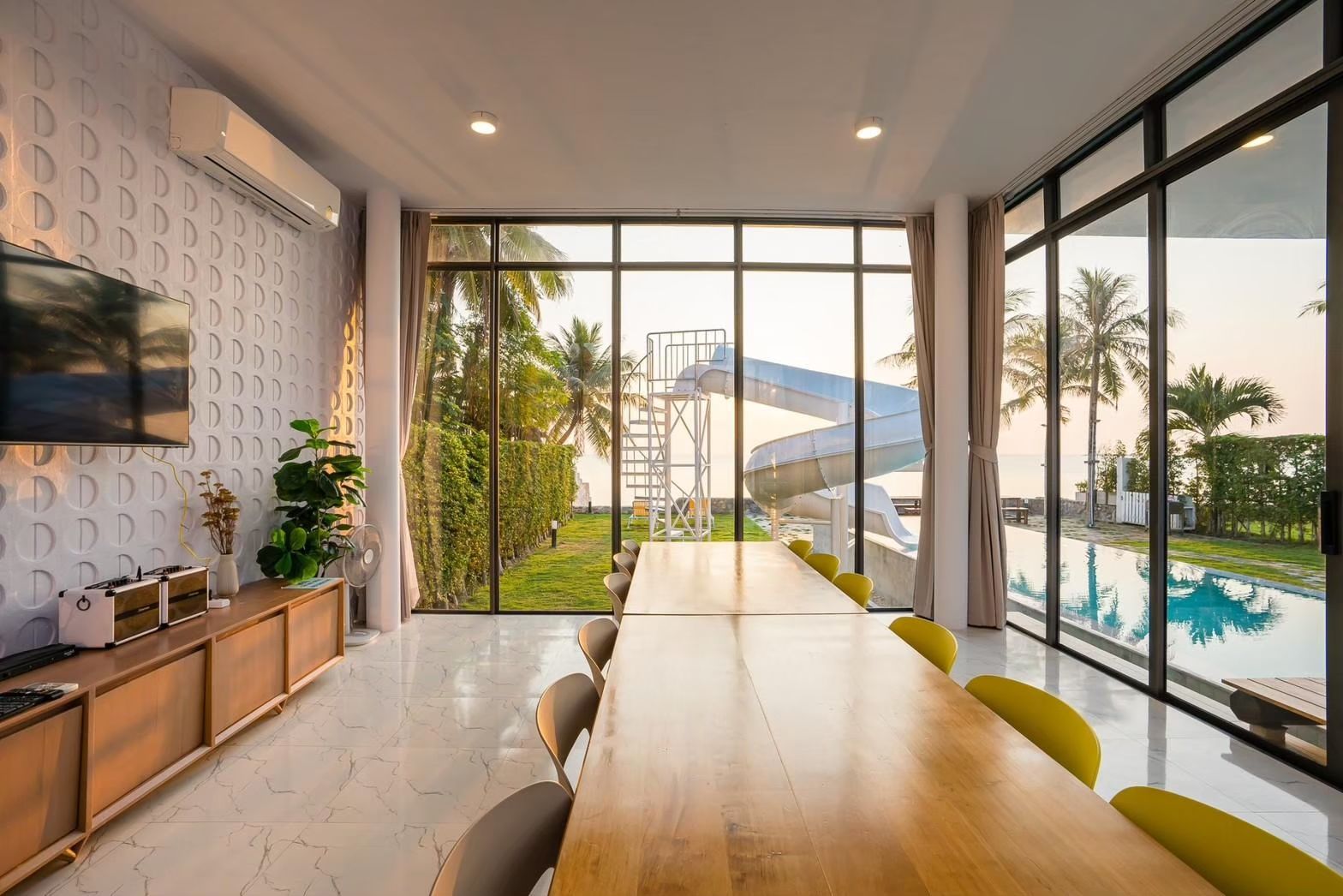 Dining area at Cross Sea VII Pool Villa, หาดคลองเทียน-ชะอำ. Long wooden table with view of pool and waterslide.