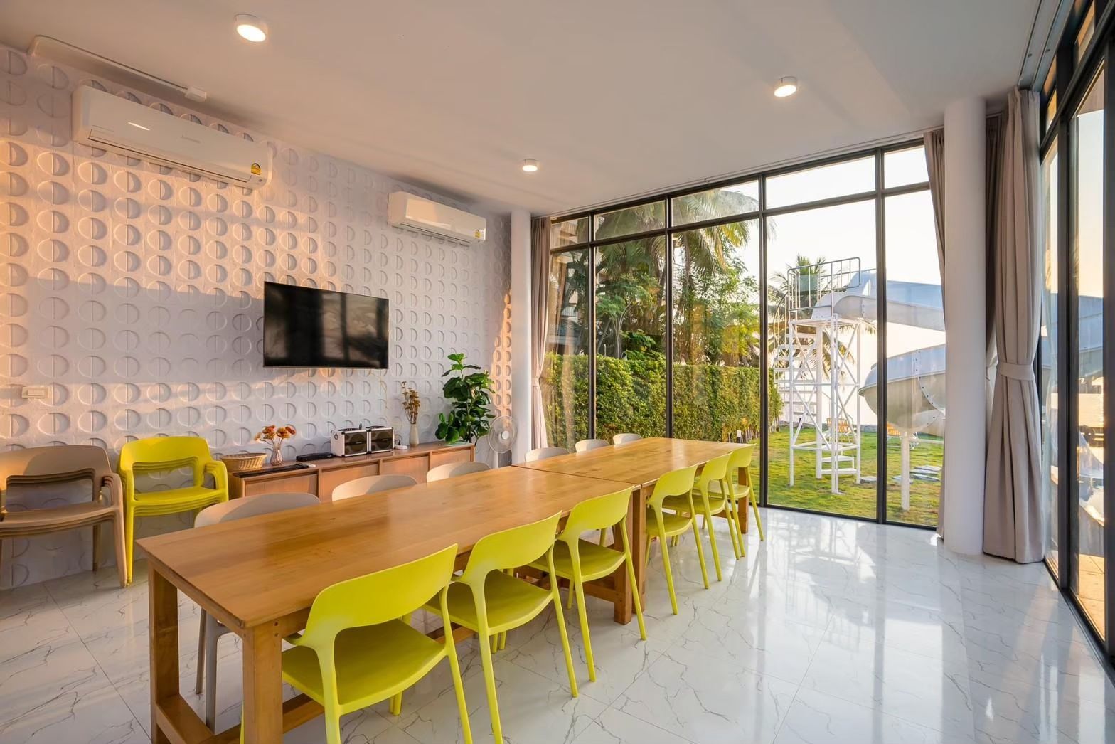 Bright dining room at Cross Sea VII Pool Villa, หาดคลองเทียน-ชะอำ. Long wooden table with yellow chairs, TV, and view of the 