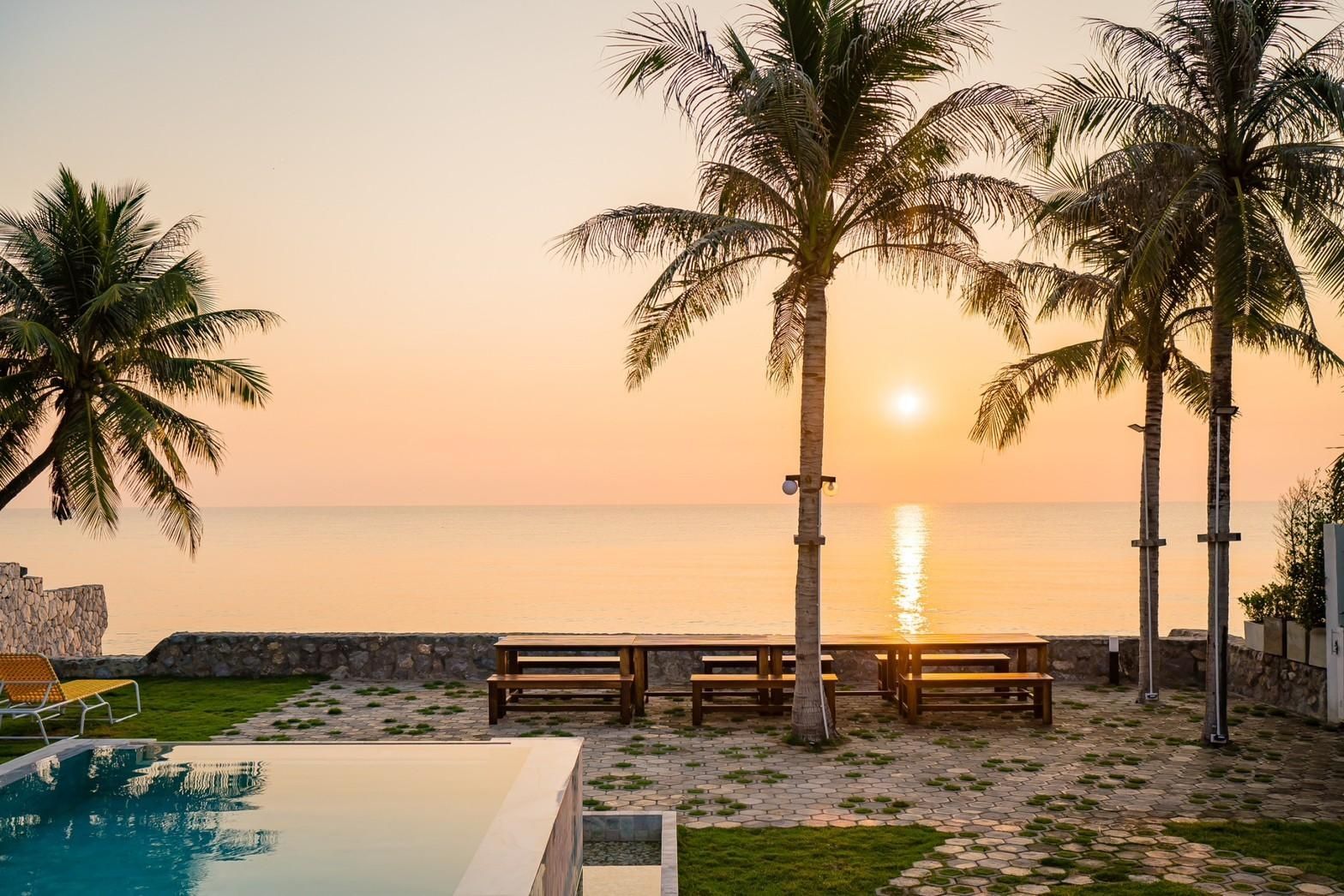 Sunset view from the pool at Cross Sea VII Pool Villa, หาดคลองเทียน-ชะอำ. Palm trees and ocean view.