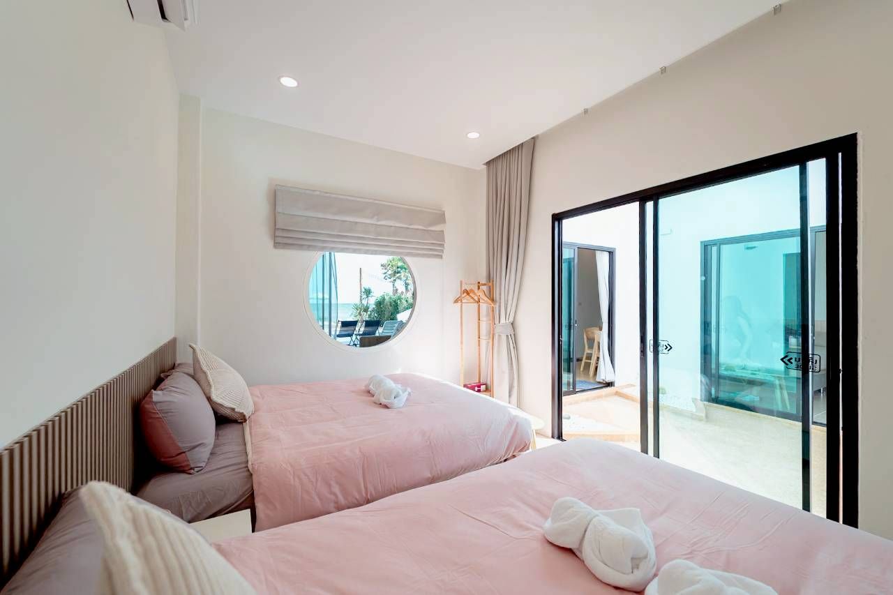 Darlington IV Pool Villa bedroom with twin beds, round window with ocean view, and sliding glass doors.