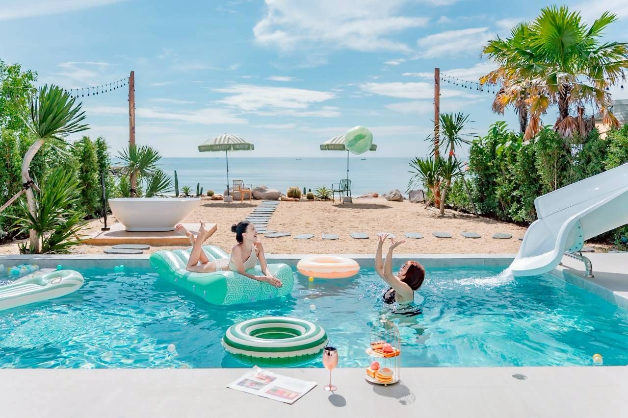Darlington IV pool villa beachfront pool with waterslide. Women relaxing on floats in Hua Hin, Thailand.