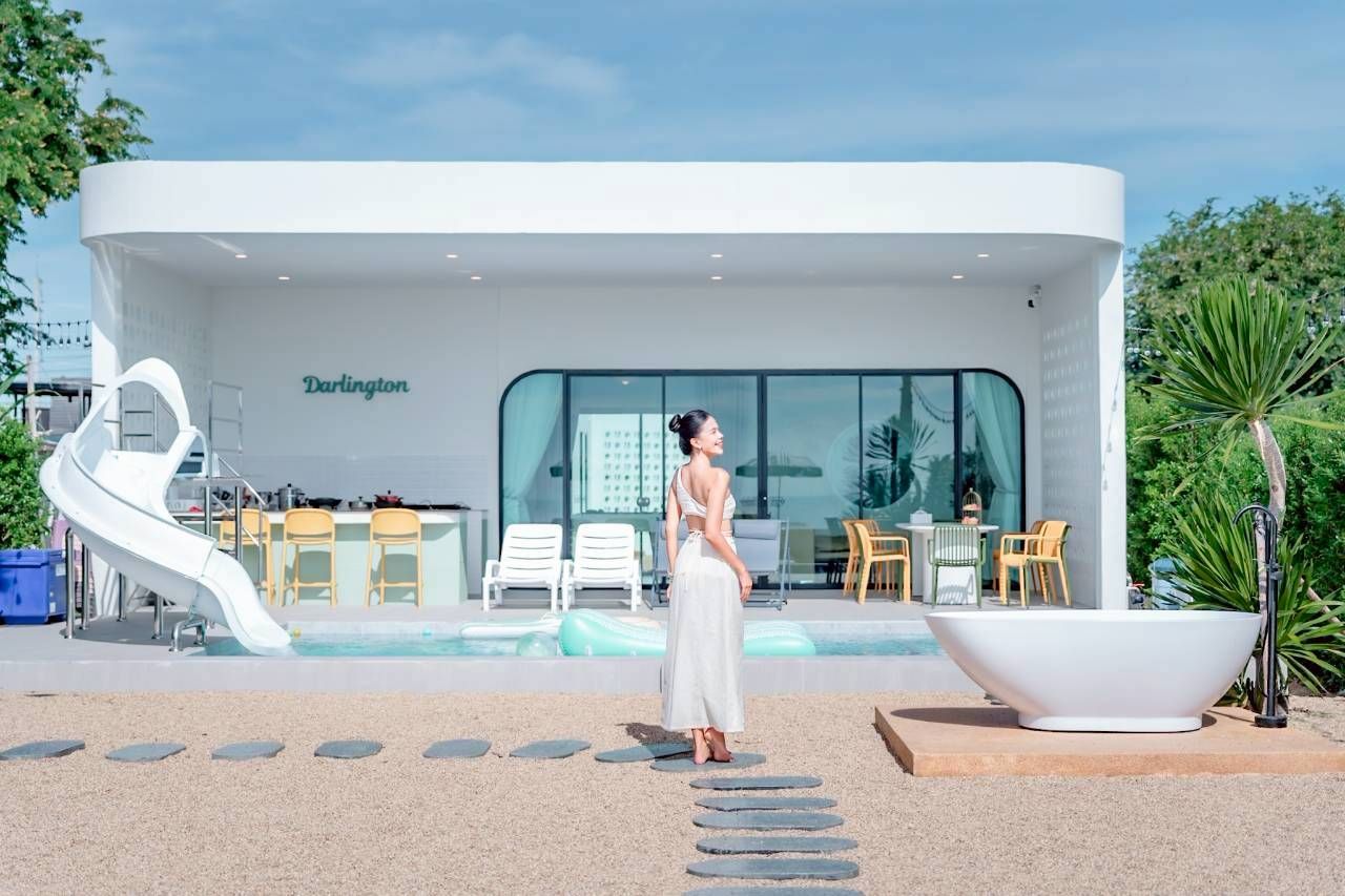 Darlington IV pool villa view with water slide, outdoor bathtub, and poolside bar. Woman standing on stone path.