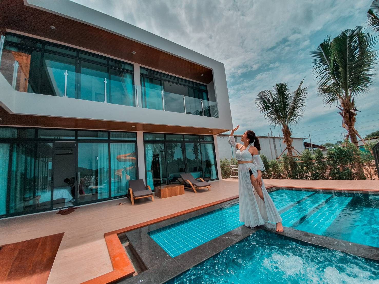 Woman in white dress at Exclusive Proud VI Villa pool in Hua Hin. Modern villa with pool and palm trees.