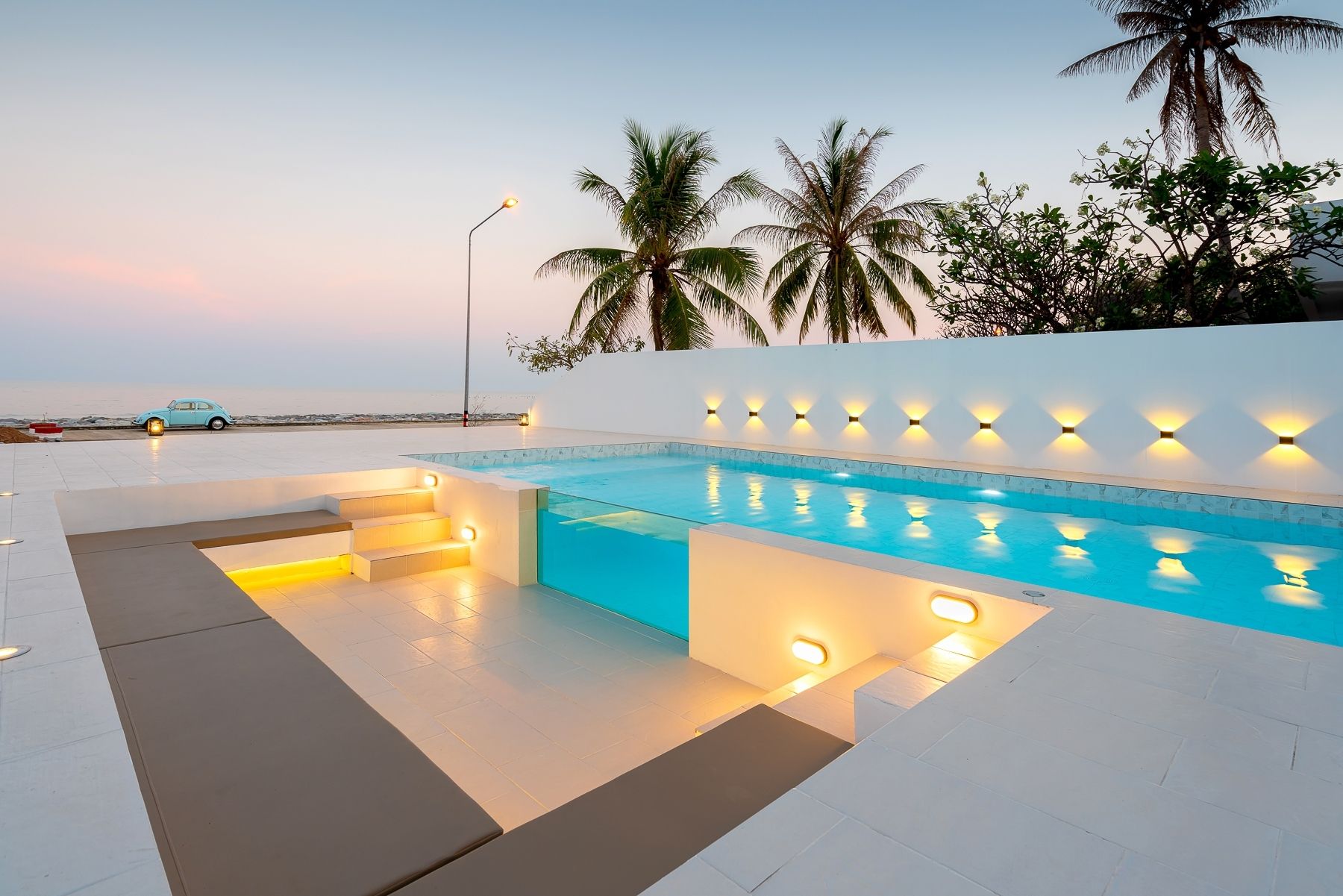 G Villa III pool villa in Pak Nam Pran, Pranburi. View of the pool with glass panel and built-in seating area at dusk.