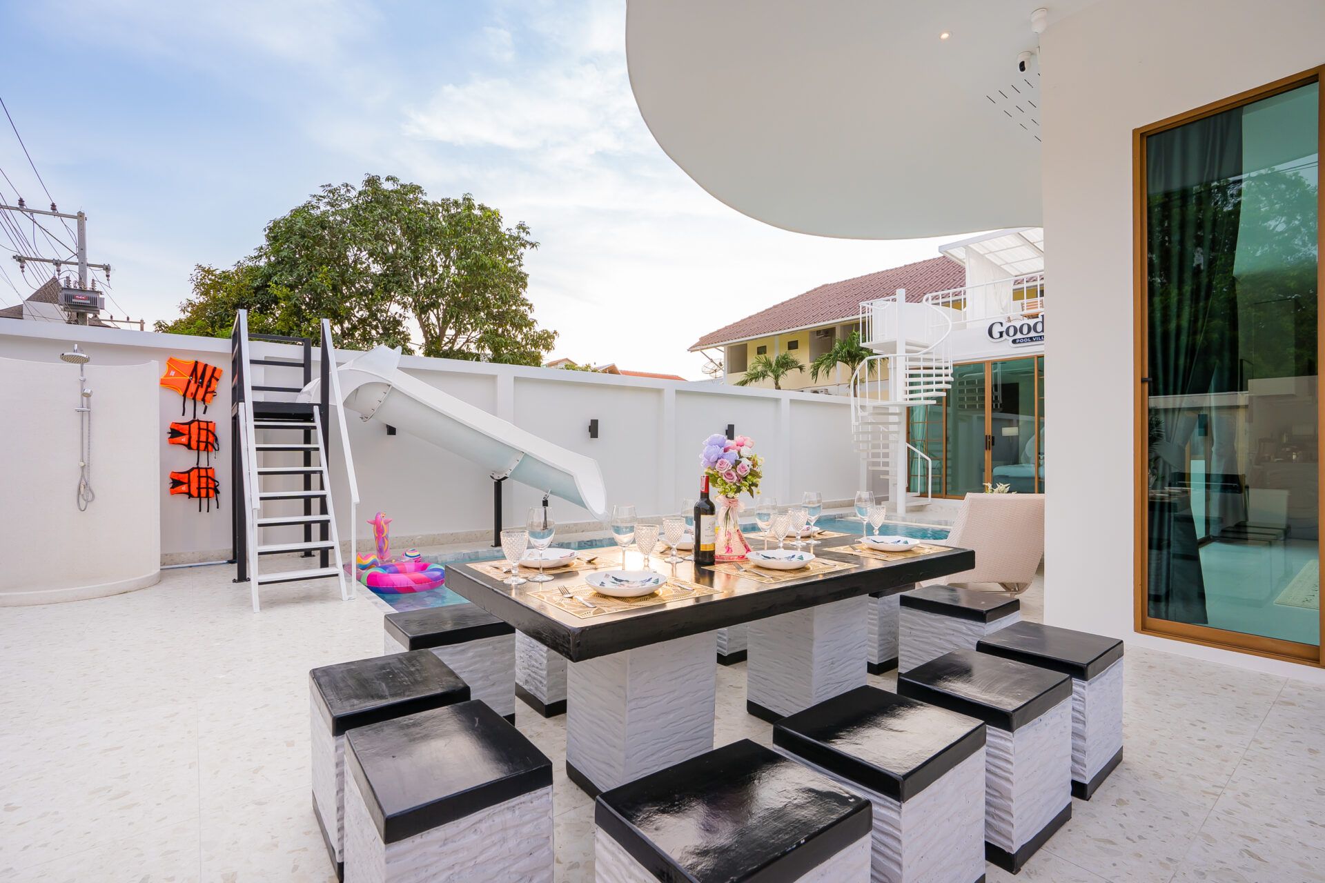 Poolside dining table set for a meal at Good Day V Pool Villa, South Pattaya. View of the pool and waterslide.