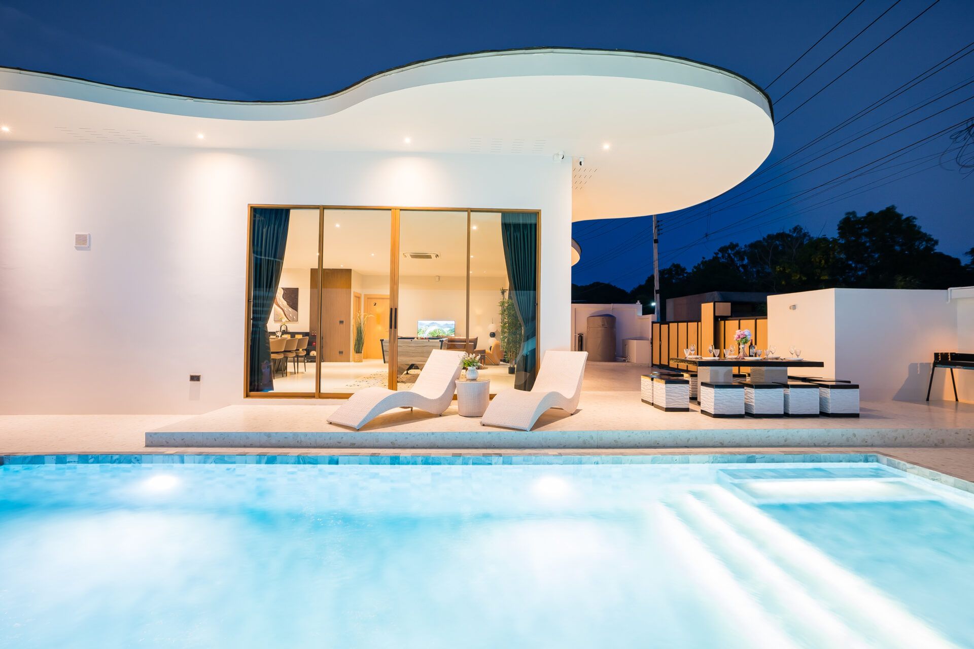 Good Day V Pool Villa in Jomtien, South Pattaya. View of the pool with lounge chairs and outdoor dining at dusk.