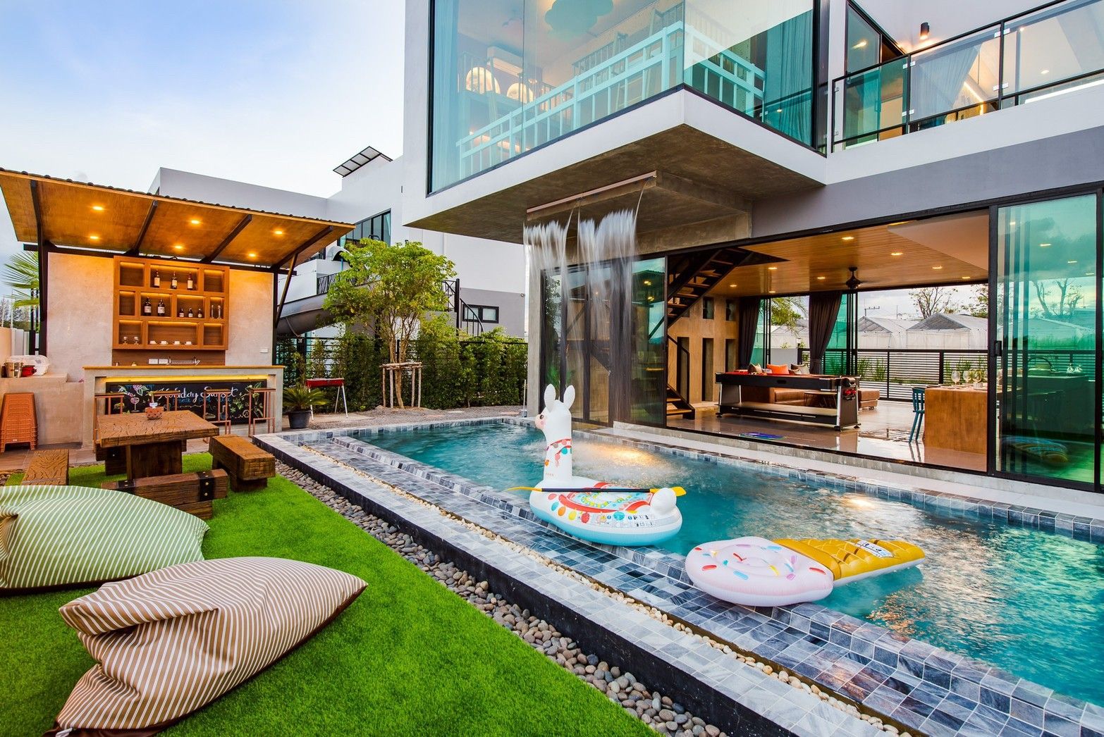 Holiday Sunset Villa IV pool with waterfall feature and swim-up bar, Hua Hin. Pool floats and beanbag chairs visible.