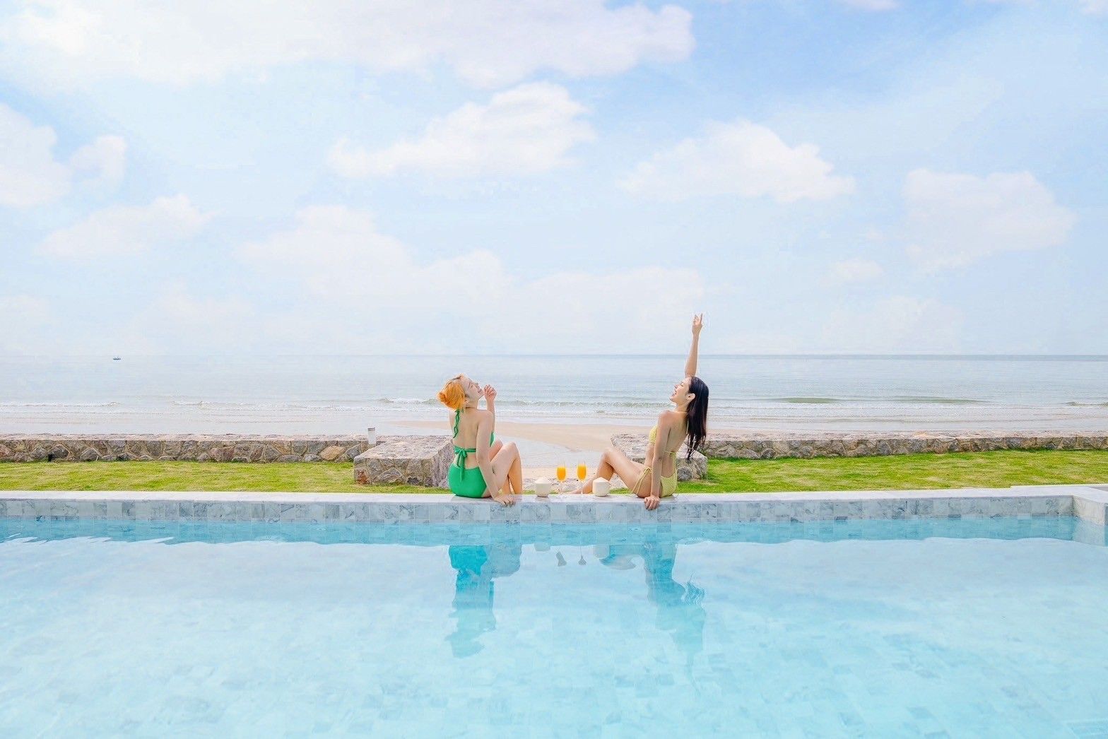 Two women relax poolside at Pailay V Beachfront Pool Villa, ชะอำ เพชรบุรี. Enjoying drinks with ocean views.