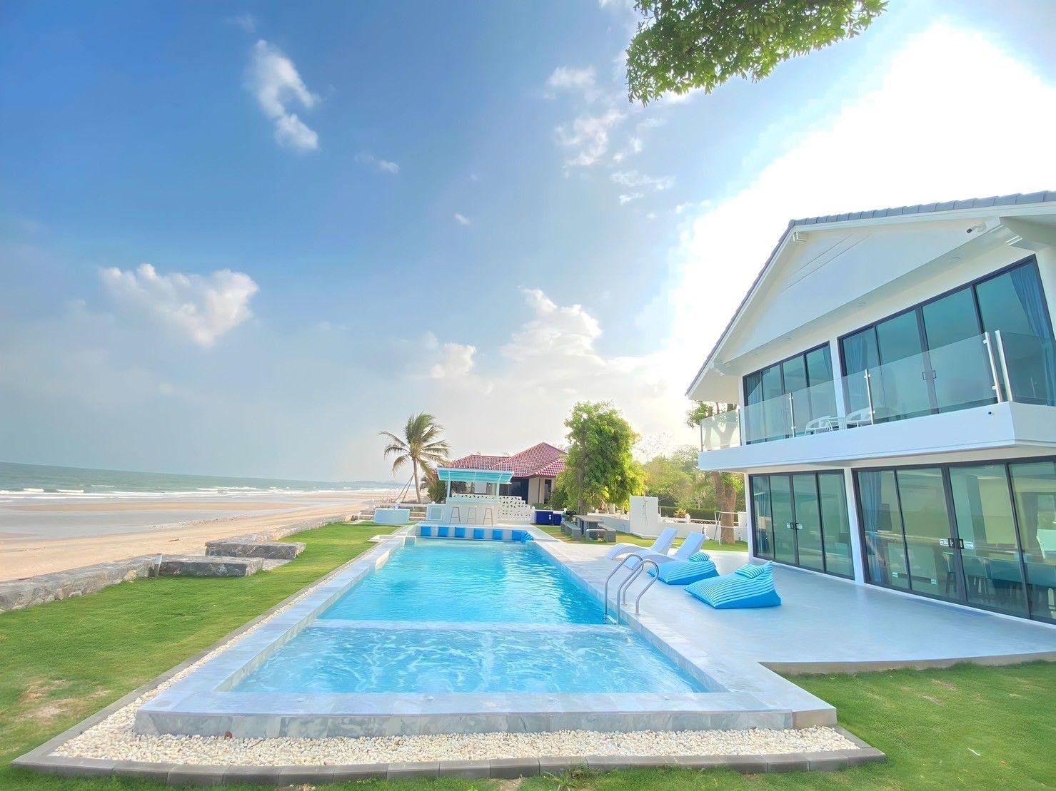 Pailay V Beachfront Pool Villa in ชะอำ เพชรบุรี. View of the pool, beach, and villa exterior on a sunny day.