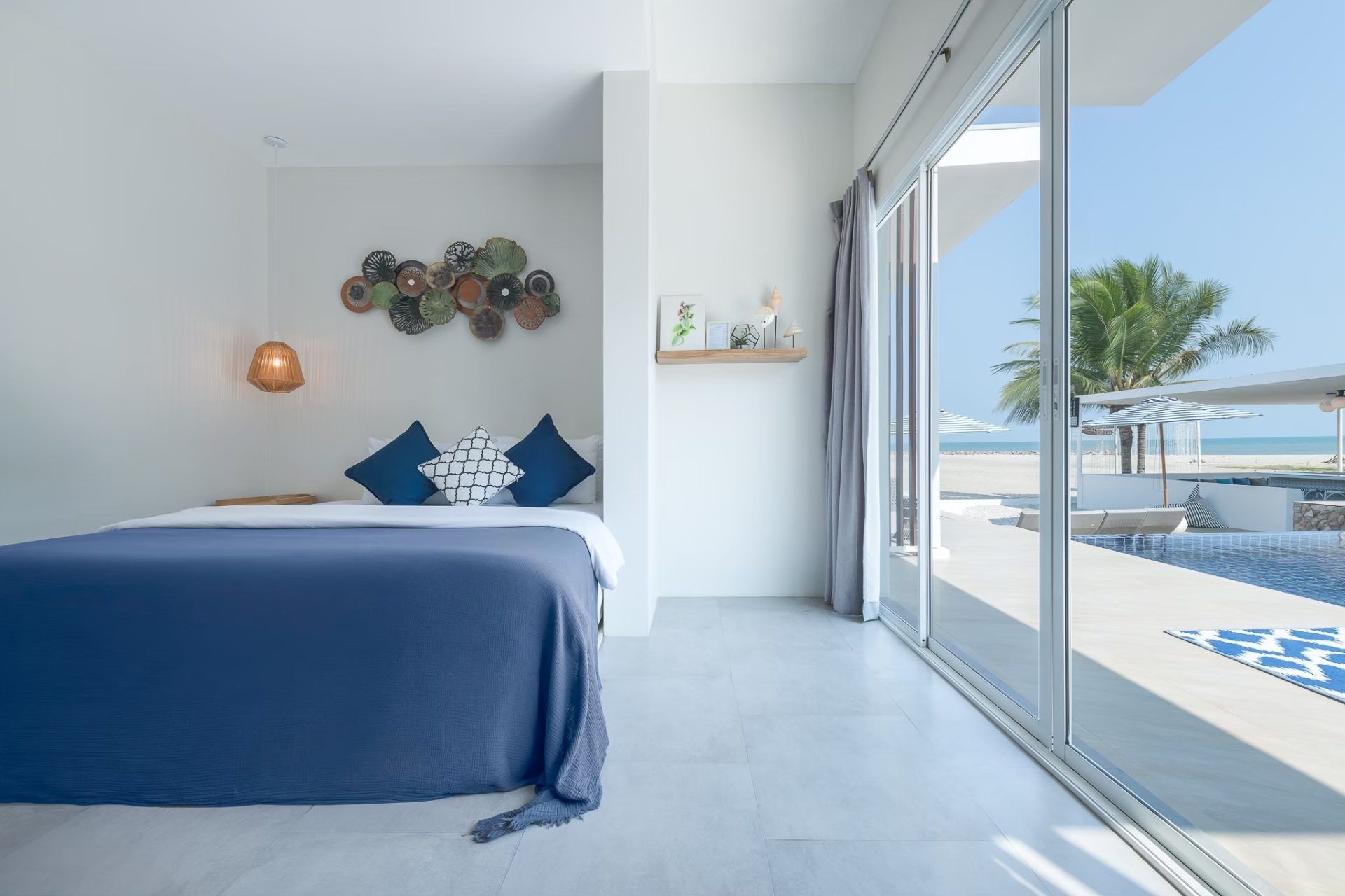Vela VI pool villa bedroom in หาดปึกเตียน ชะอำ with blue bedspread and view of the beach.