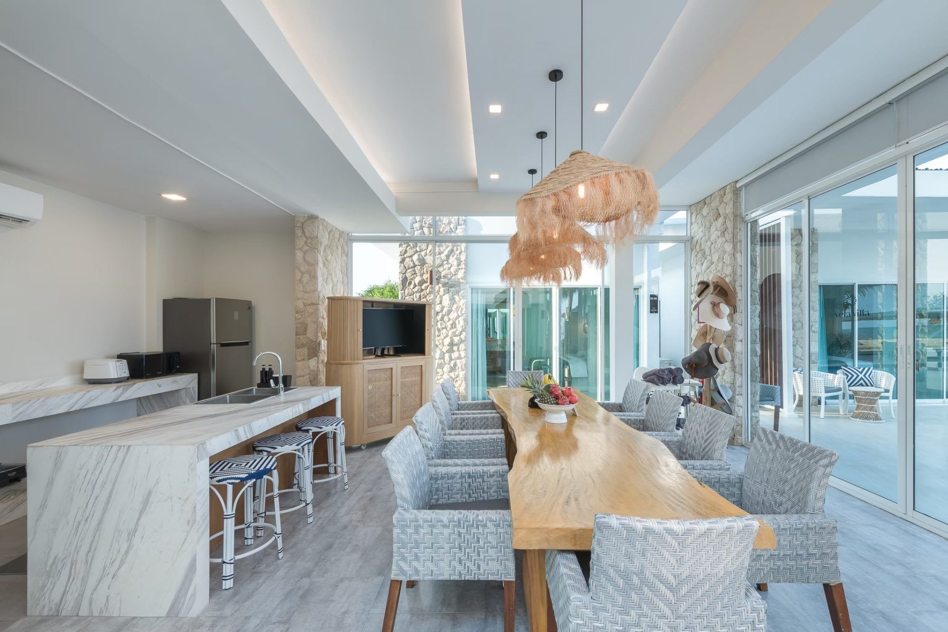 Dining area at Vela VI Pool Villa, หาดปึกเตียน ชะอำ. Long wooden table with woven chairs and unique light fixture.