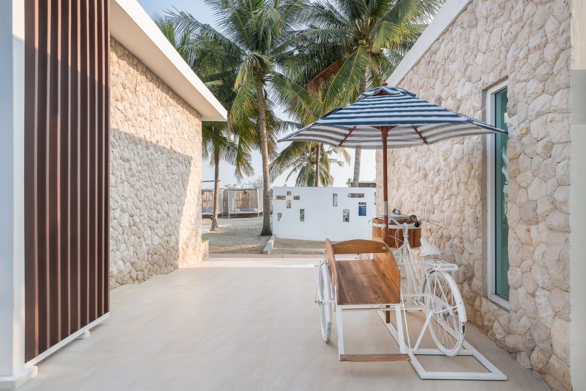 Beach access at Vela VI Pool Villa, หาดปึกเตียน ชะอำ. A white tricycle with a striped umbrella sits on the patio.