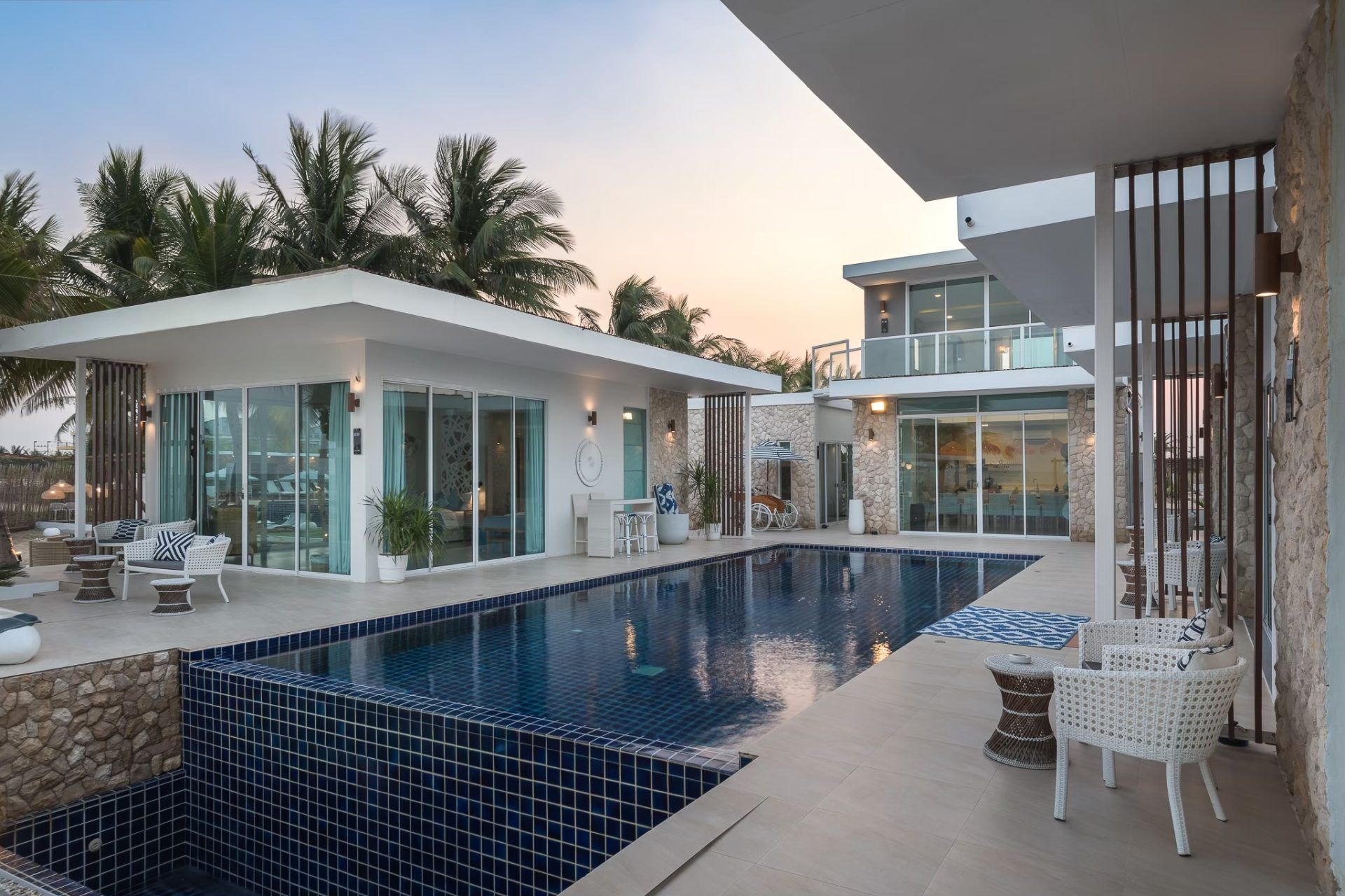Vela VI pool villa in หาดปึกเตียน ชะอำ features a dark blue tiled swimming pool and outdoor seating areas.