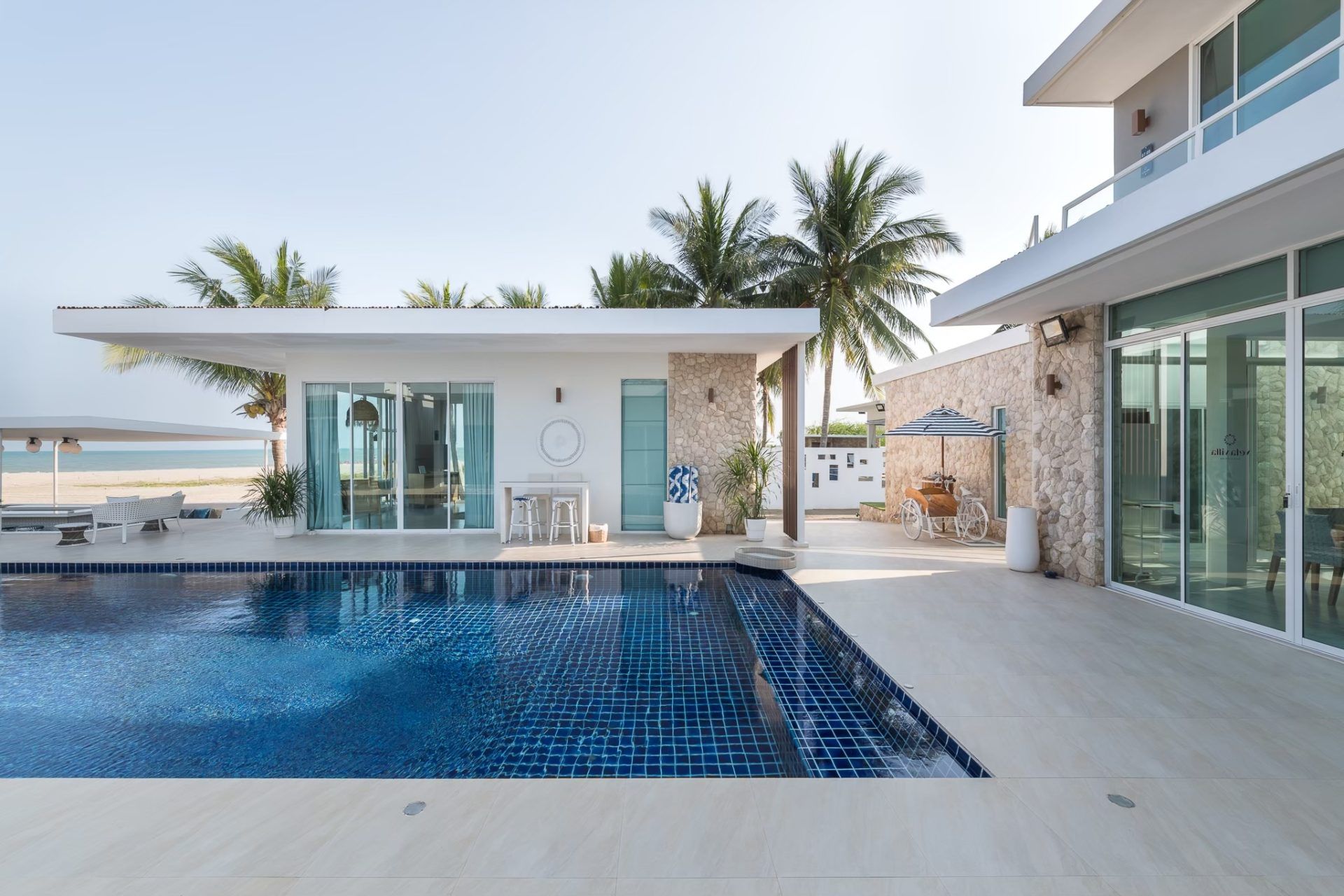 Sparkling blue tiled pool at Vela VI Pool Villa, หาดปึกเตียน ชะอำ. View of the villa and beach beyond.
