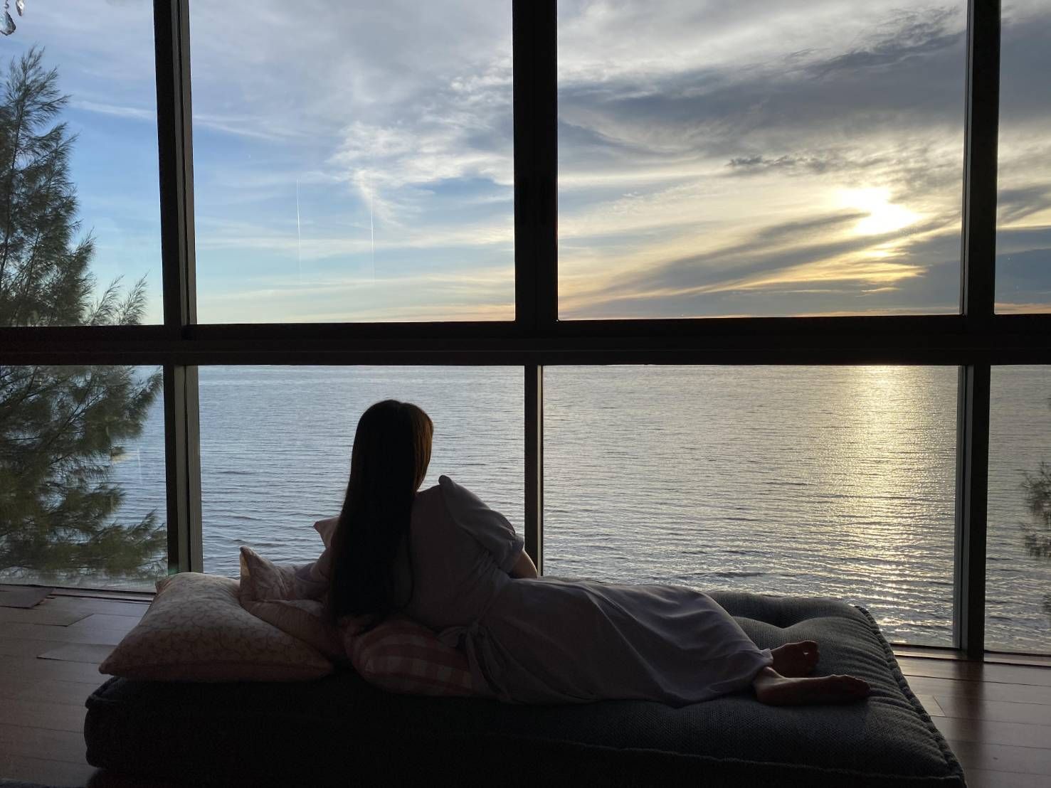 Ocean view from Pink Sand Beachfront Villa in Pattaya. Woman relaxing on daybed by large window overlooking the sea.