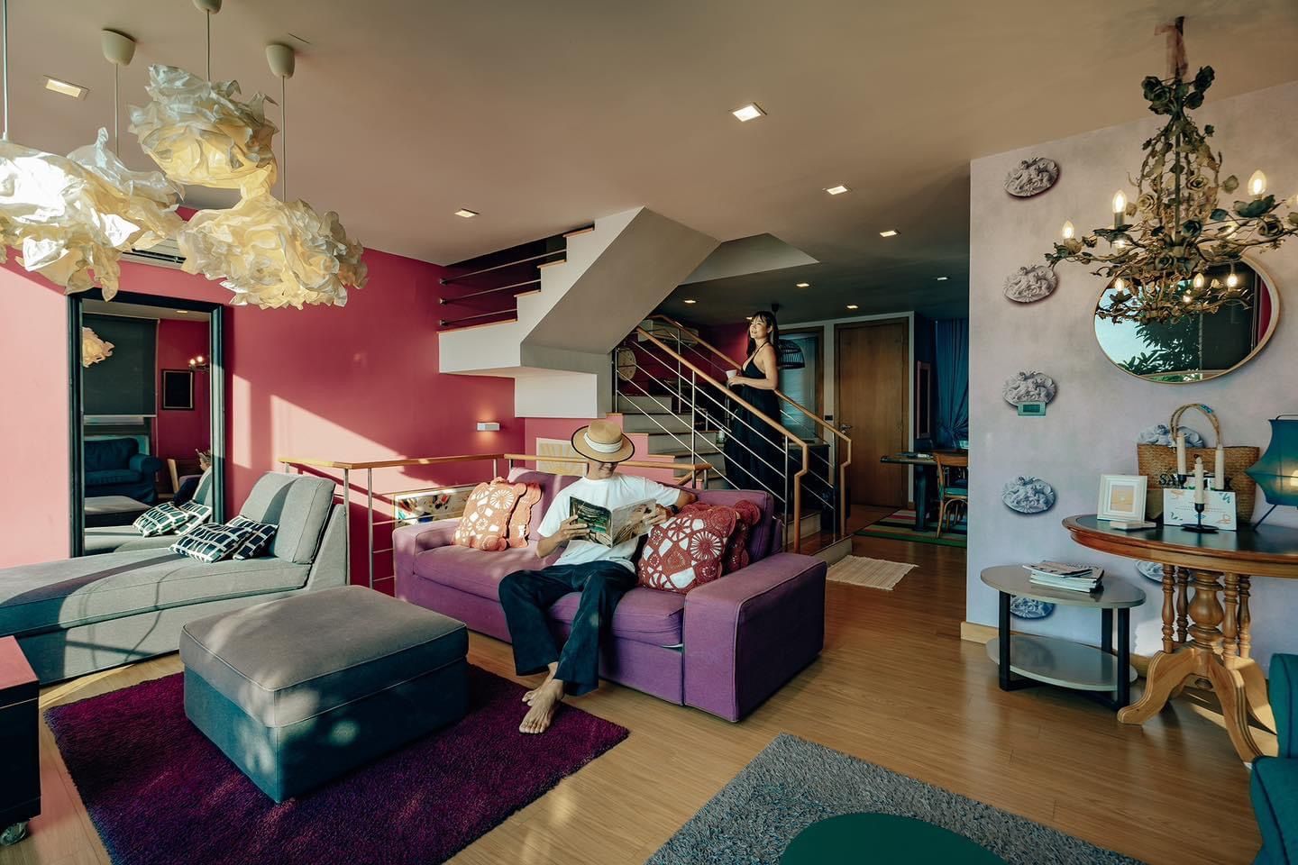 Living room at Pink Sand Beachfront Villa, บางละมุง พัทยาเหนือ. Man reading on purple sofa, stairs to upper level.