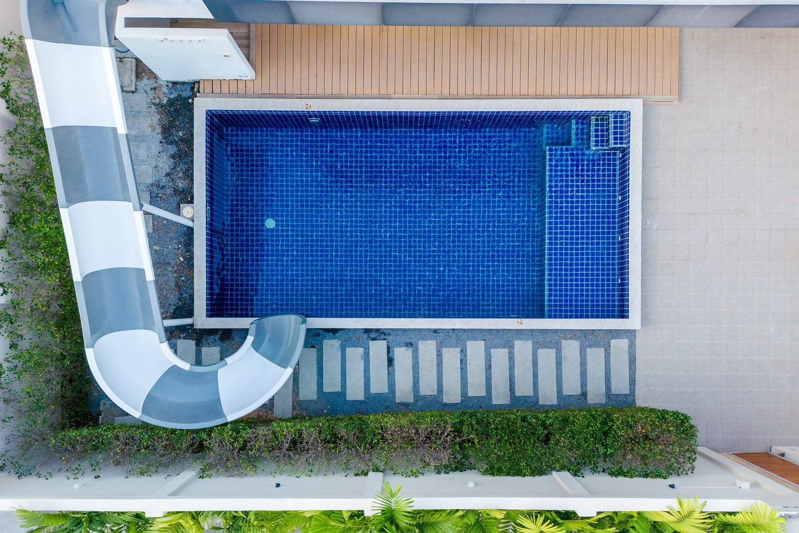 Aerial view of the pool and waterslide at Pool Lay A IV Pool Villa, นาจอมเทียน-ห้วยใหญ่ พัทยาใต้. Blue tiled pool with steps.