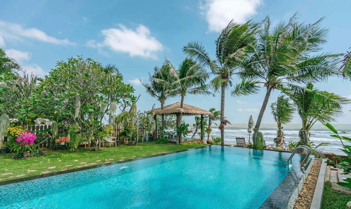 Oceanfront pool at Pran Beach Villa I, เขากะโหลก ปราณบุรี. View of the ocean and a thatched roof cabana from the pool.