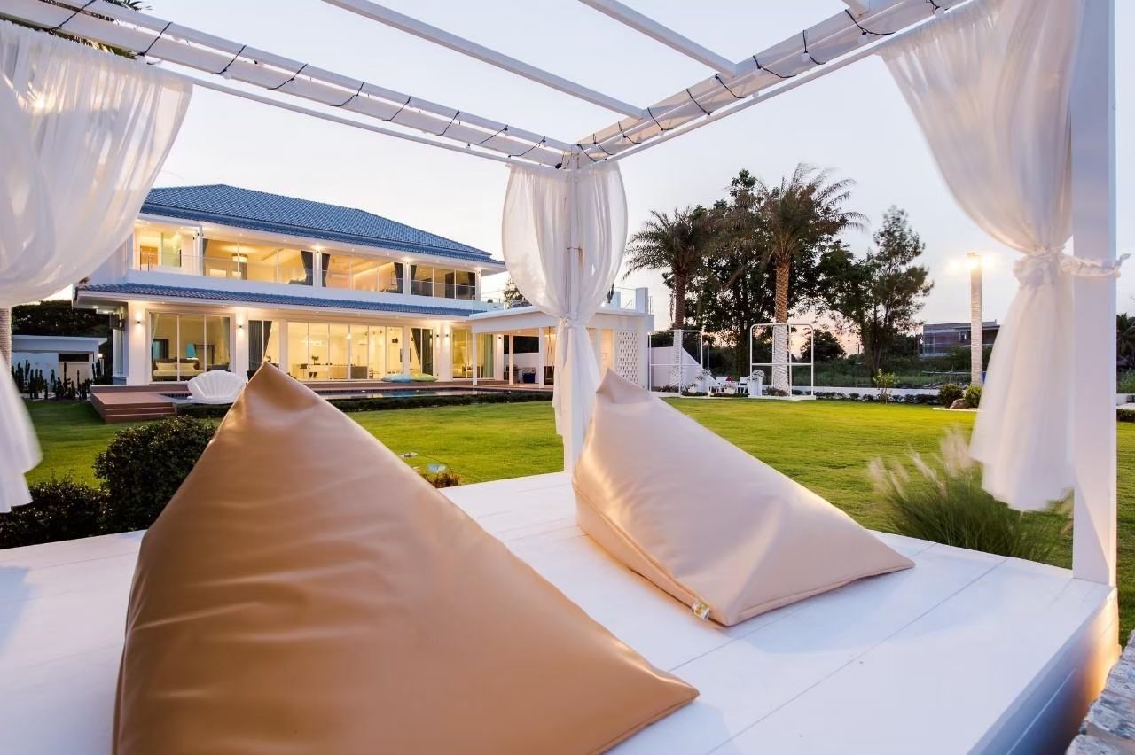 Relax on beanbag chairs under a pergola at Private Heaven VI pool villa, Cha-Am. View of the lawn and villa exterior.