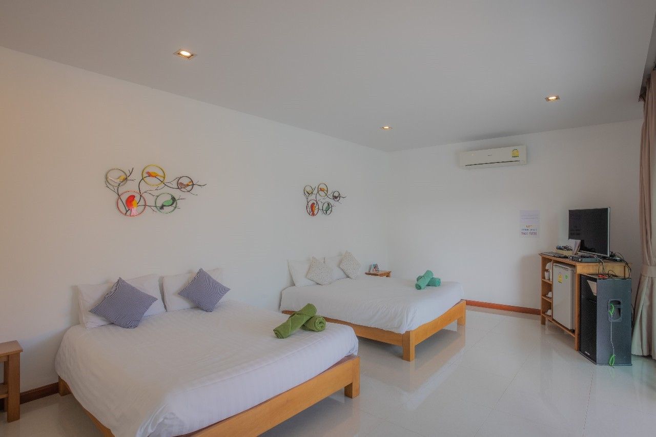 Bright bedroom with two beds at Proud II Pool Villa, Hua Hin. White walls, colorful bird art, and a TV for relaxing.