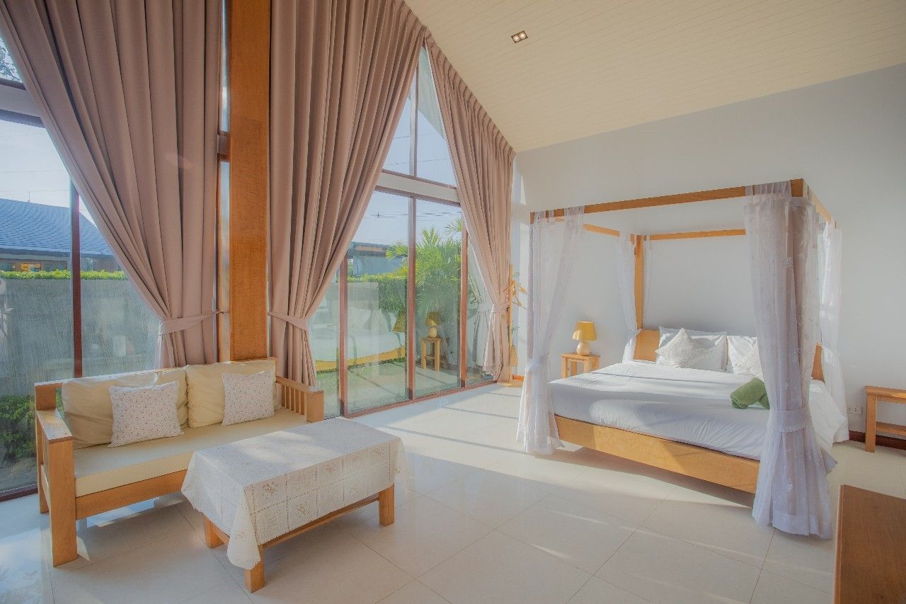 Bright bedroom suite with four-poster bed at Proud II Pool Villa, Hua Hin. Large windows and comfortable seating area.