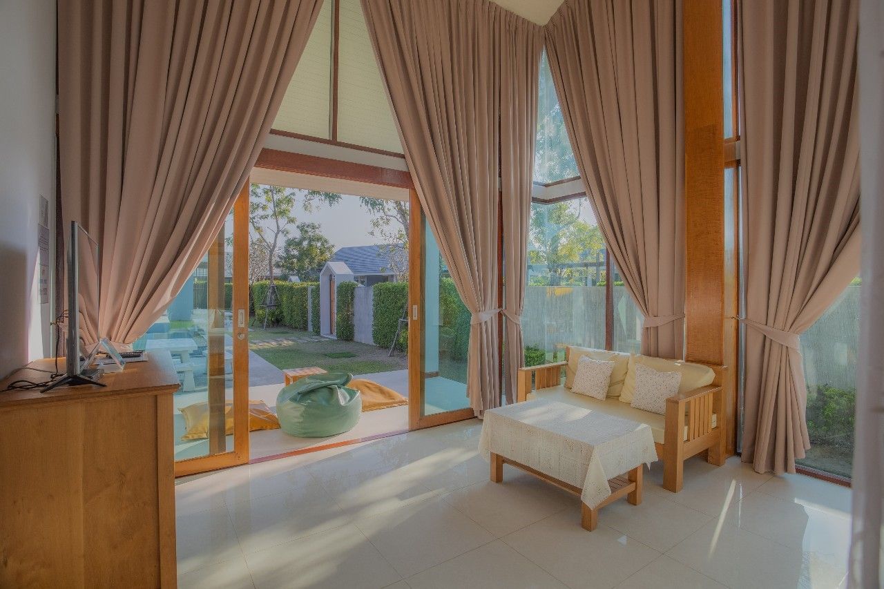 Bright living area with garden view at Proud II Pool Villa, Hua Hin. Relax in luxury with natural light and comfortable seati