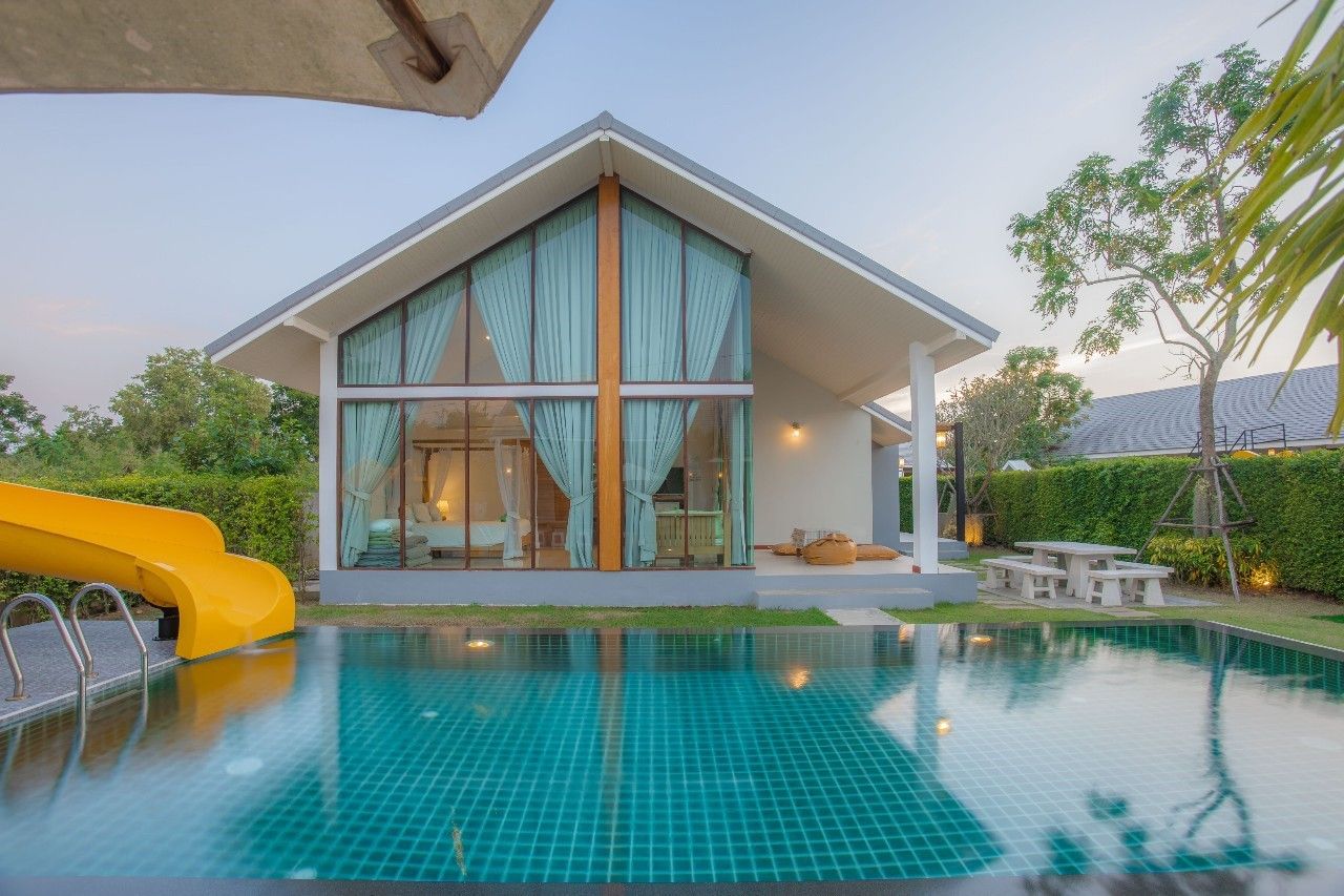 Proud II Pool Villa Hua Hin pool view with waterslide and bedroom visible through large windows.