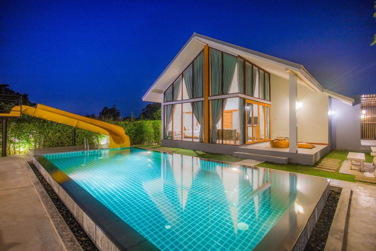 Night view of the pool and slide at Proud II Pool Villa, Hua Hin. Modern villa with large windows reflecting in the pool.
