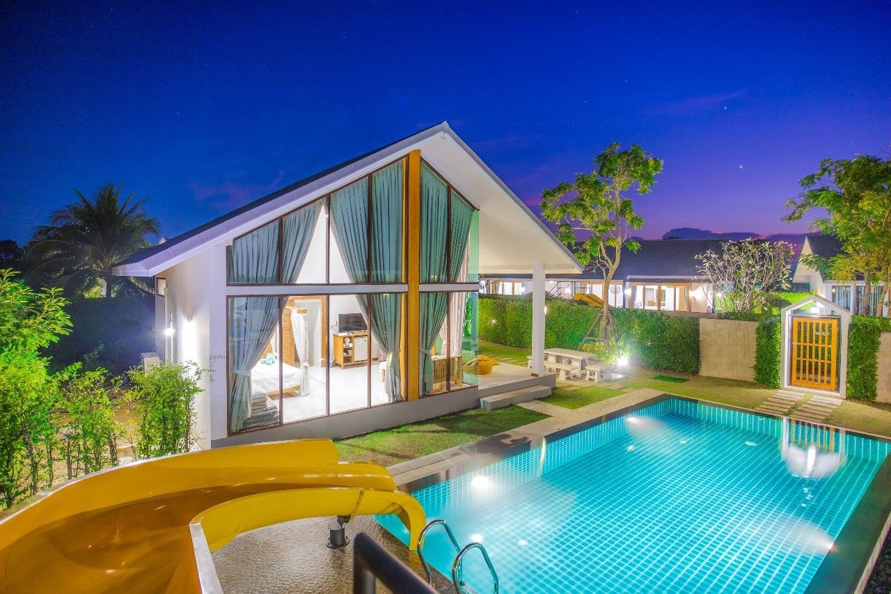 Night view of the pool and waterslide at Proud II Pool Villa, Hua Hin. Bedroom visible through large windows.