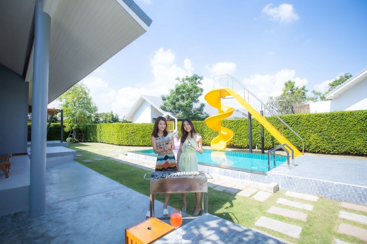 Poolside BBQ at Proud III Pool Villa, Hua Hin. Two women grilling by the pool with a yellow water slide.