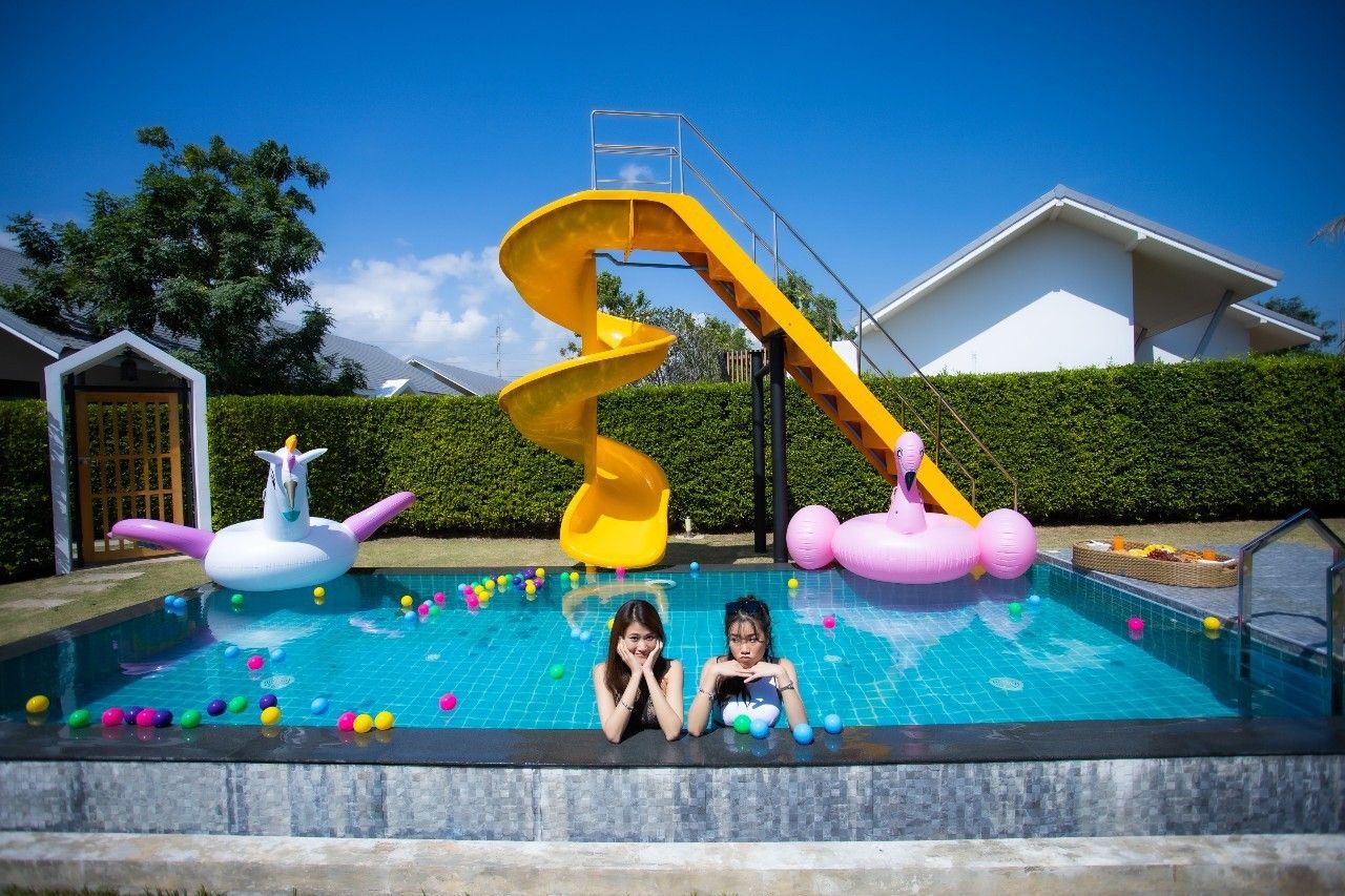 Fun pool scene at Proud III Pool Villa, Hua Hin. Features a yellow slide, unicorn and flamingo inflatables, and colorful ball