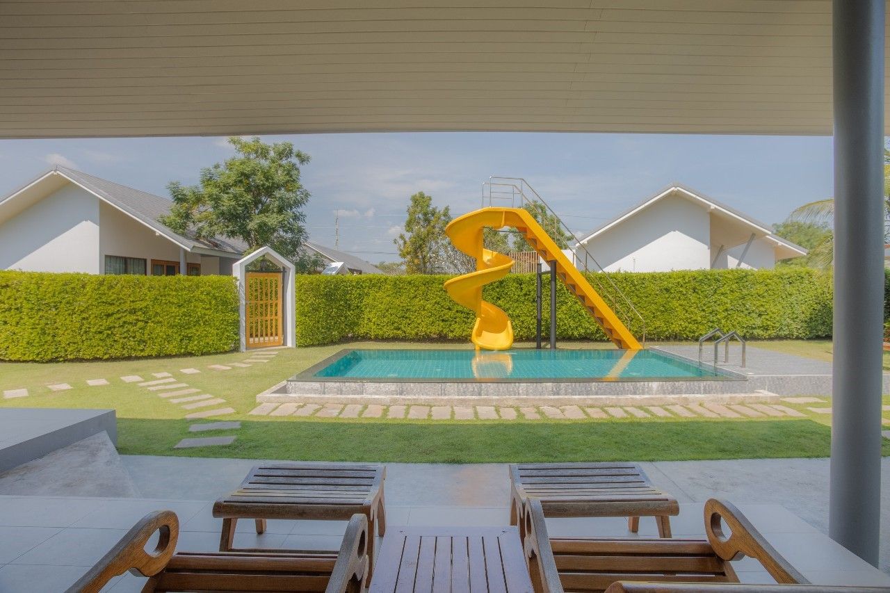 Swimming pool with yellow slide at Proud III Pool Villa, Hua Hin. View from patio with lounge chairs.