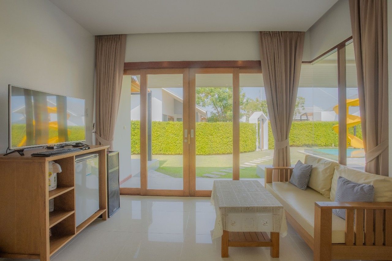 Bright living room with pool view at Proud III Pool Villa, Hua Hin. Sofa, TV, and garden access.